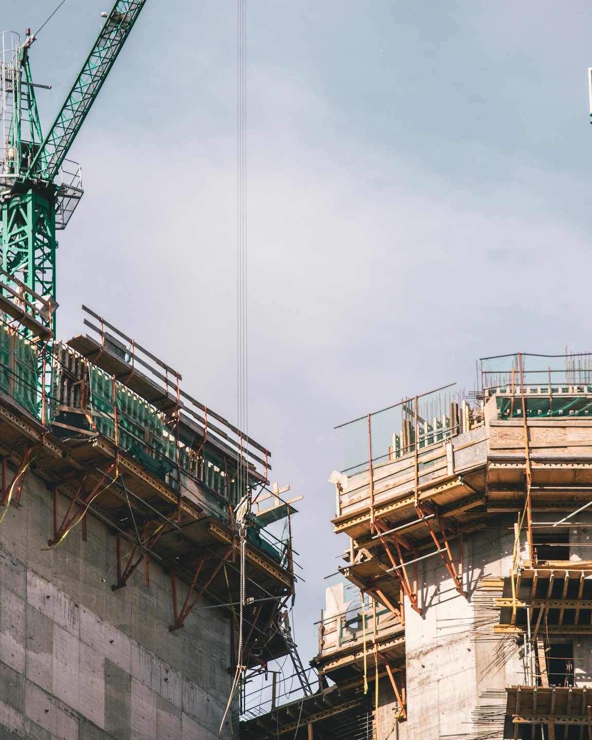 Two unfinished concrete buildings with scaffolding and a crane.